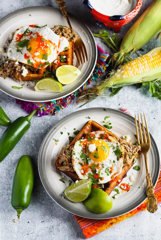 black bean and corn waffle on a small plate topped with a sunny side up egg and cilantro and a side of lime