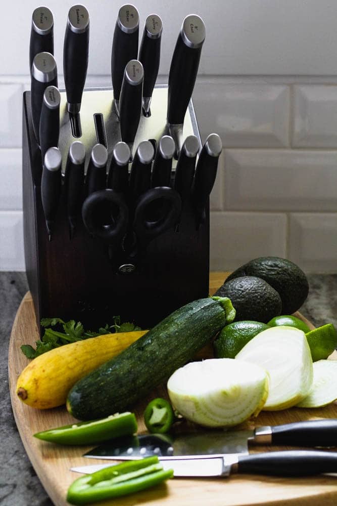 cutting board filled with jalapenos, onion, squash and avocado before preparing for the recipe alongside a Calphalon self-sharpening knife set