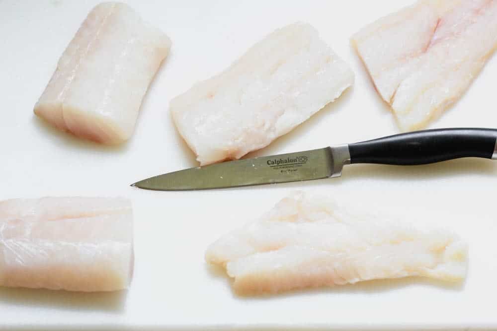 raw cod on a while plastic cutting board with a Calphalon knife