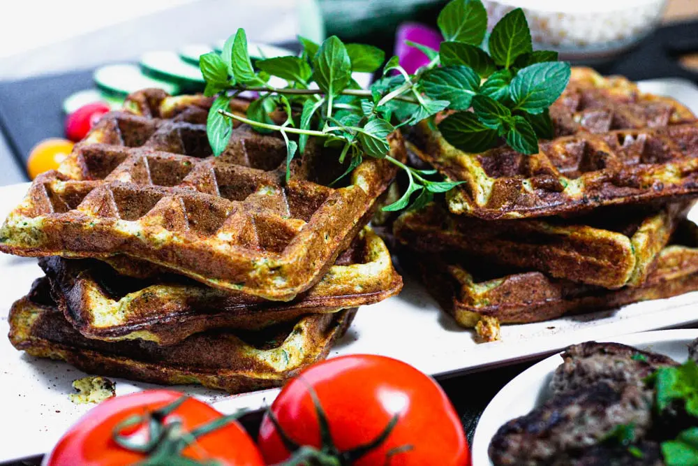 falafel waffles topped with fresh mint and surrounded by red onions, tomatoes and lamb sausage