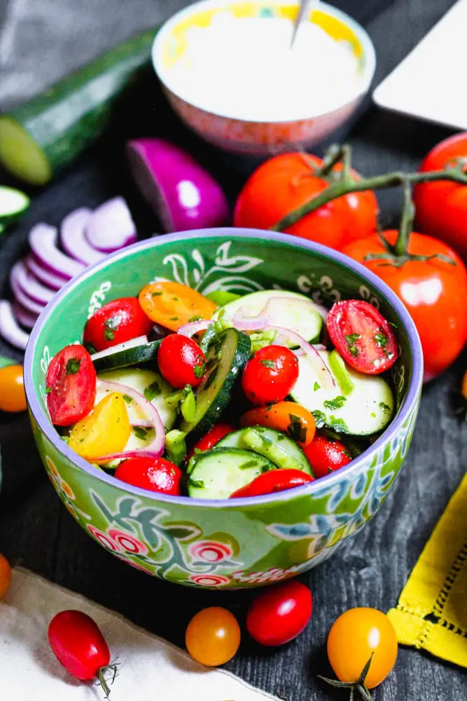 cucumber tomato salad in a green bowl with a small bowl of yogurt sauce in the background