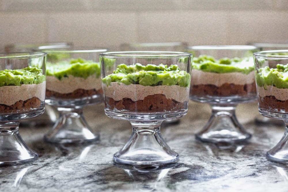 Beginning of seven layer dip prep with the first three layers place in individual trifle dishes
