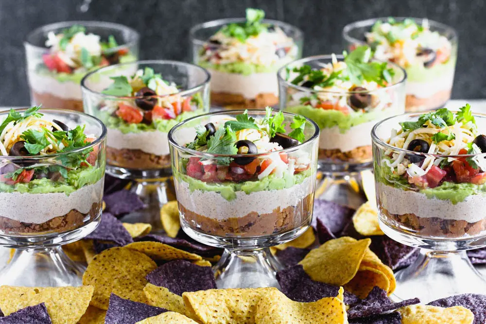 individual sever layer dips in small trifle dishes with blue and yellow corn tortilla chips scattered around