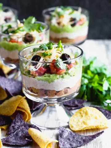 individual sever layer dips in small trifle dishes with blue and yellow corn tortilla chips scattered around
