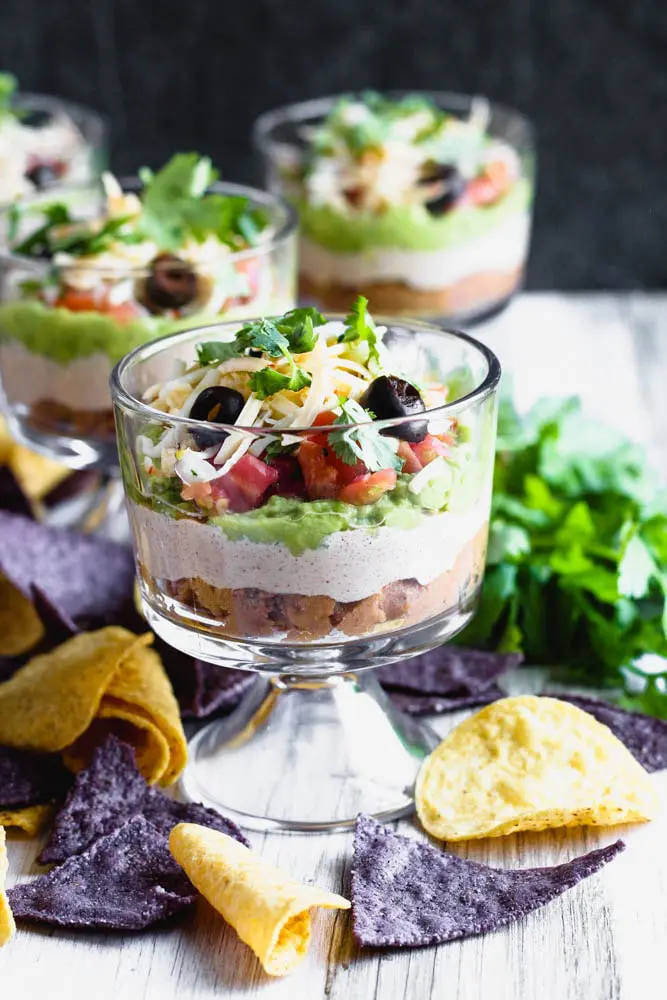 individual sever layer dips in small trifle dishes with blue and yellow corn tortilla chips scattered around