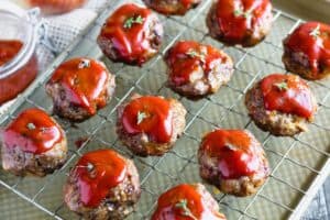 Mini meatloaf dressed in a ketchup based dressing on a sheet pan line with a cooling rack