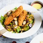 Bowl of salad topped with roasted broccoli, sliced grapes and almonds and shredded cheese with a side of honey mustard