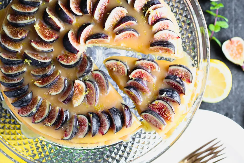 closeup overhead shot of lemon yogurt cake topped with honey caramel and quartered figs on a crystal cake pedestal with one slice being removed