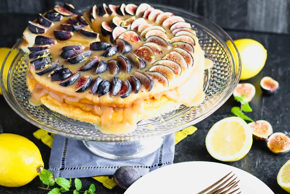 emon yogurt cake topped with honey caramel and quartered figs on a crystal cake pedestal with lemons and figs in the background