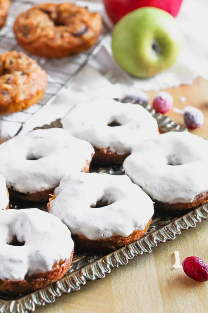 Close up shot of pumpkin donuts with a heavy layer of cream cheese glaze on a antique bronze tray with more donuts before icing on a cooling rack in the background