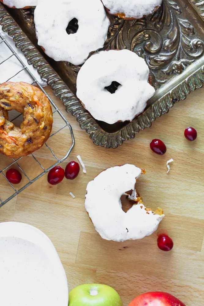 Overhead photo of table that includes a bronze antique tray with glazed pumpkin donuts, a cooling rack with unglazed donuts and one donut with a bite taken out of it