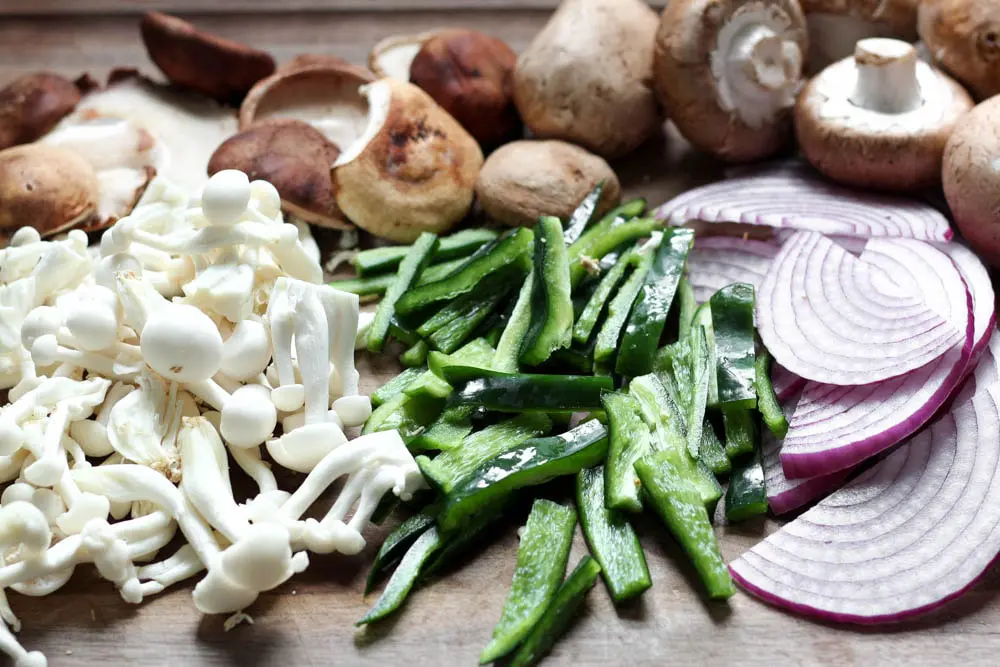 uncooked brown and white mushrooms aside piles of sliced green pepper and sliced red onion