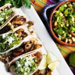 A platter of tacos garnished with arugula and corn salad beside a bowl of the same salad