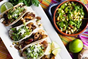 A platter of tacos garnished with arugula and corn salad beside a bowl of the same salad