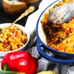 a pasta, squash, corn, and red pepper casserole in a blue baking dish with a serving of the casserole in a bowl to the side