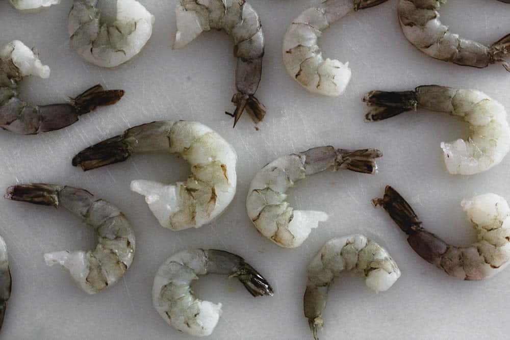 uncooked shrimp scattered on a white cutting board