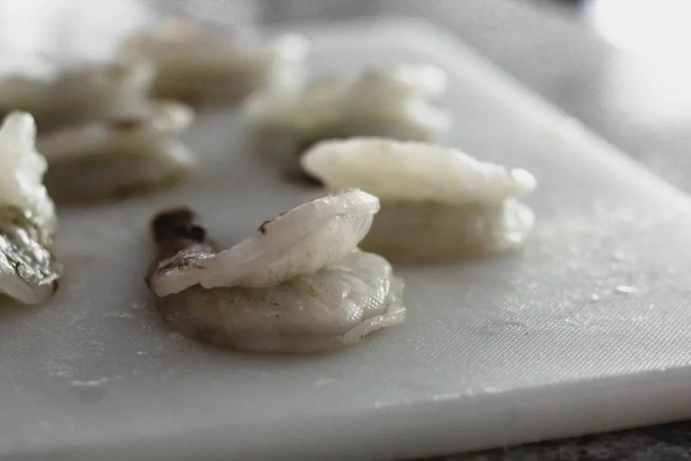 side view of an uncooked deveined shrimp on a cutting board