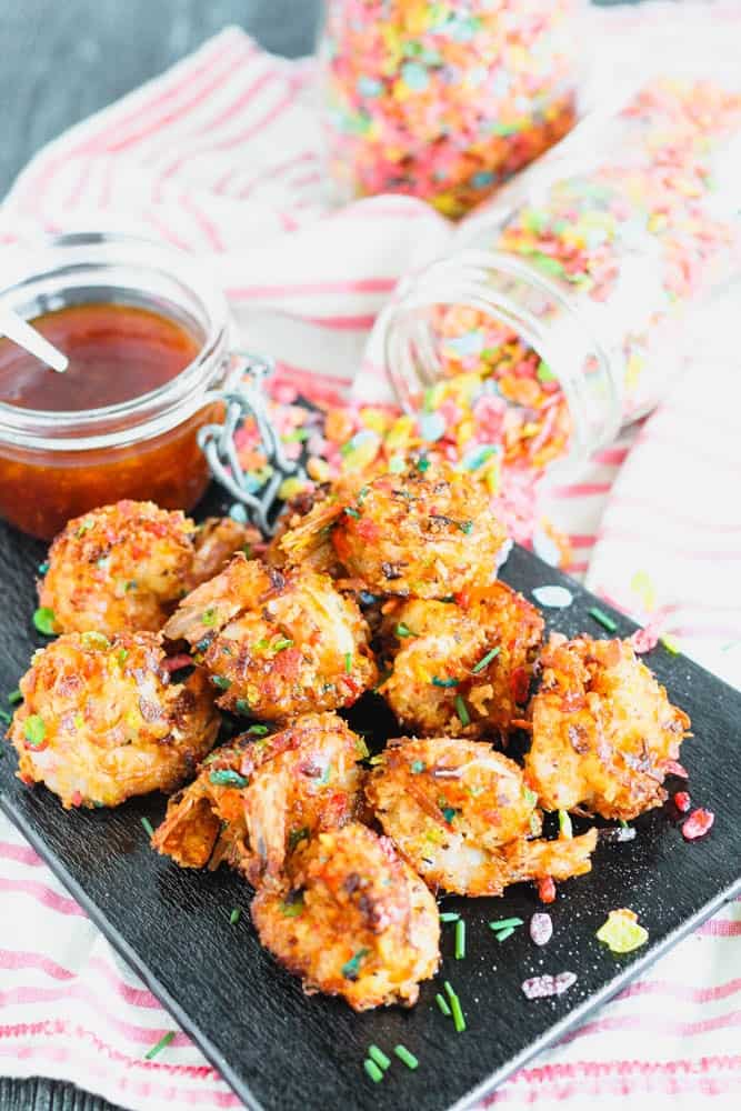 cereal coated cooked shrimp on a black board with a jar of orange dipping sauce