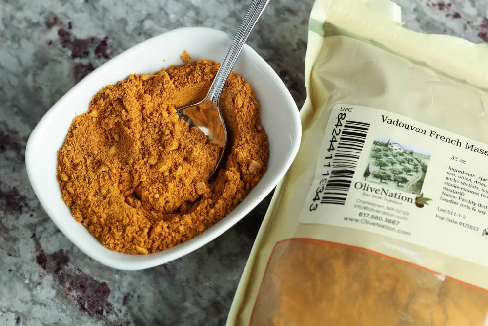 small white dish filled with orange curry powder with a silver spoon next to a bag of curry powder