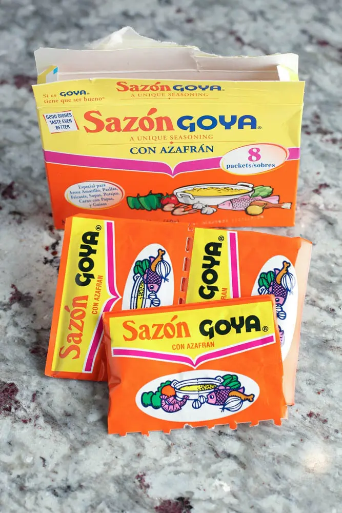 package of Sazon Con Azafran seasoning with three packets of seasoning taken out of the box