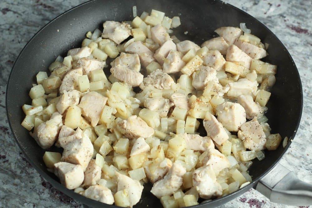 white cooked chicken breast pieces with diced potatoes and onions in a large round black skillet