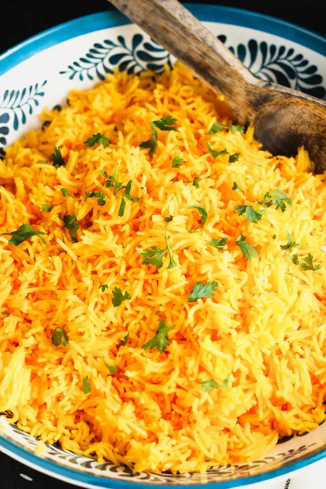 large decorative blue and white bowl with orange rice and a wooden spoon