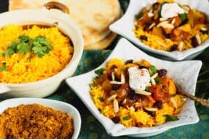 two star shaped dishes filled with orange rice and red chicken curry topped with green cilantro and white dollop of yogurt and a beige bowl filled with orange rice