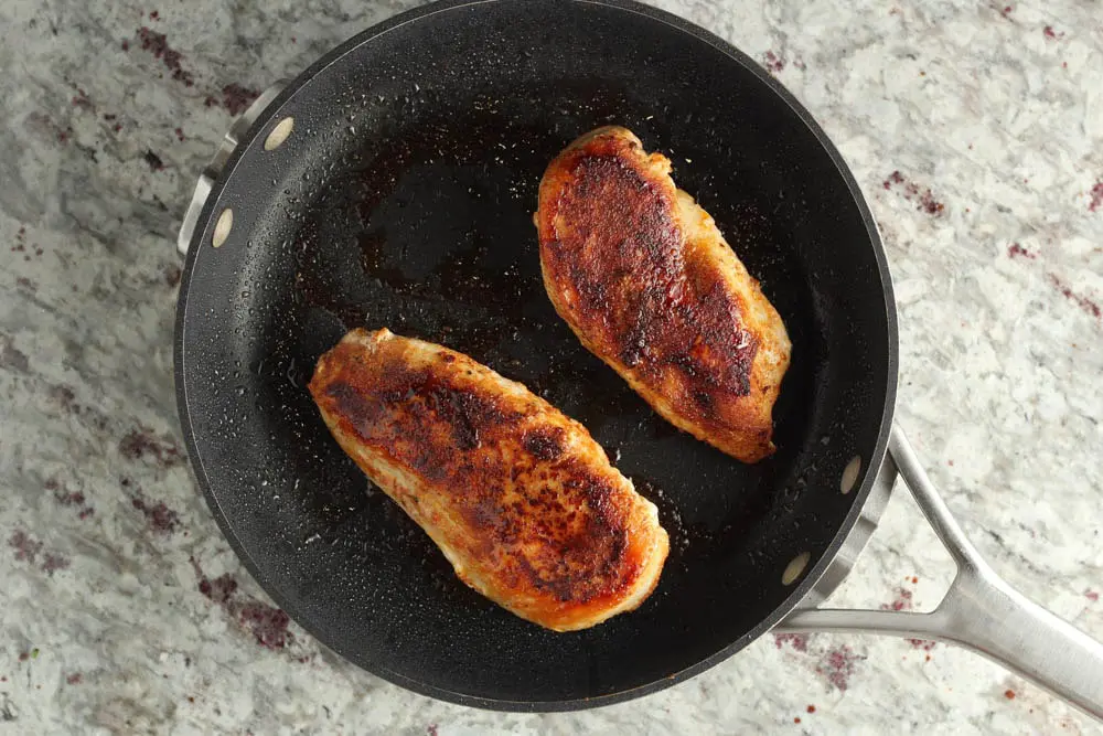 seasoned chicken breasts cooked in a dark saute pan