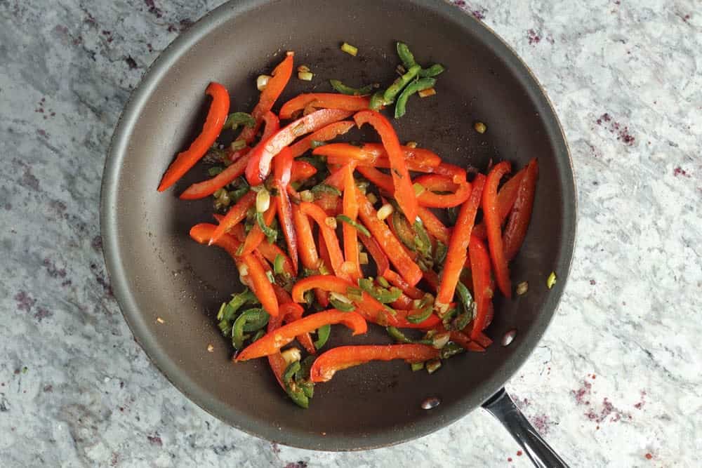 strips of red bell pepper cooking in a dark saute pan
