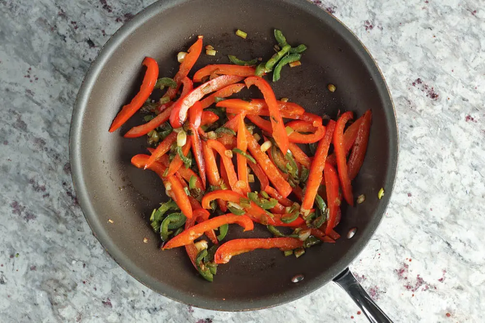 strips of red bell pepper cooking in a dark saute pan