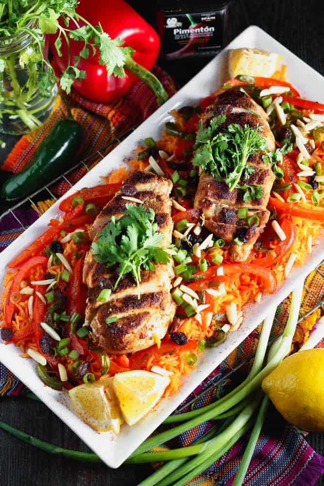 white rectangular plate filled with orange rice topped with strips of red bell pepper, green onion pieces, sliced chicken breast and cilantro