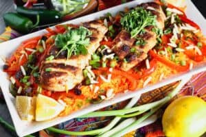 white rectangular plate filled with orange rice topped with strips of red bell pepper, green onion pieces, sliced chicken breast and cilantro