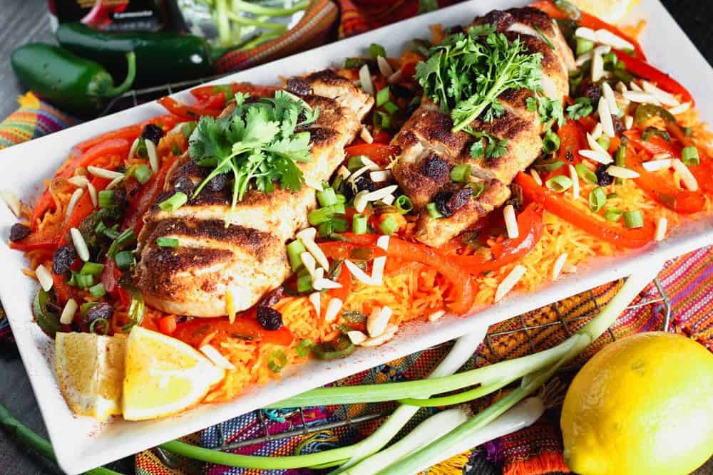 white rectangular plate filled with orange rice topped with strips of red bell pepper, green onion pieces, sliced chicken breast and cilantro
