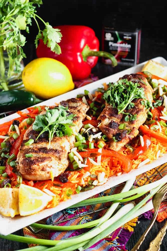 white rectangular plate filled with orange rice topped with strips of red bell pepper, green onion pieces, sliced chicken breast and cilantro
