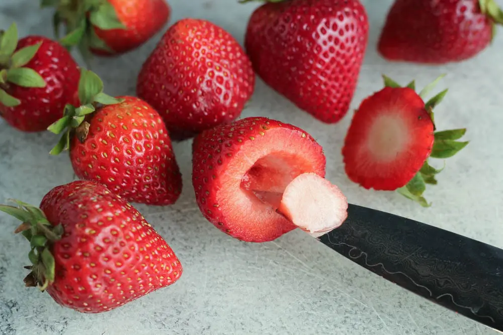 close up of strawberries on a clear cutting board with one strawberry demonstrating how to hill a strawberry