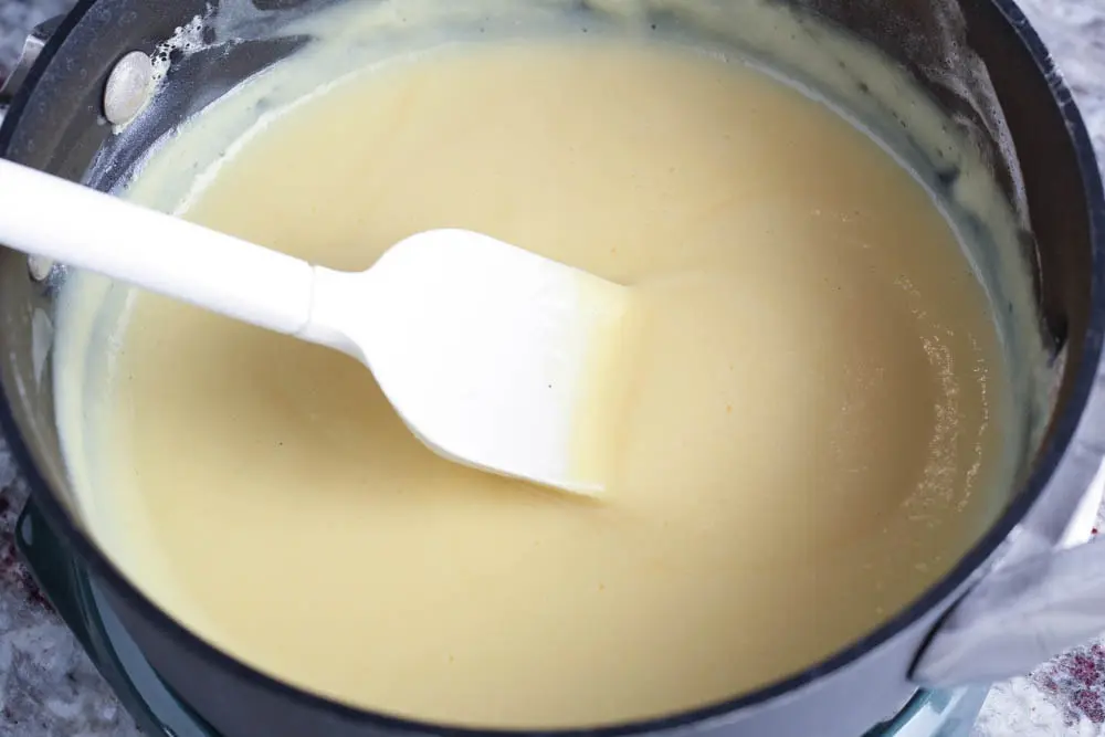 pale yellow vanilla pudding in a saucepan after reaching the desired consistency with a white spatula stirring