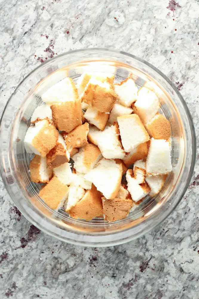 overhead view of brown and white angel food cake pieces in a round clear glass trifle fish as the first layer of Strawberry Trifle