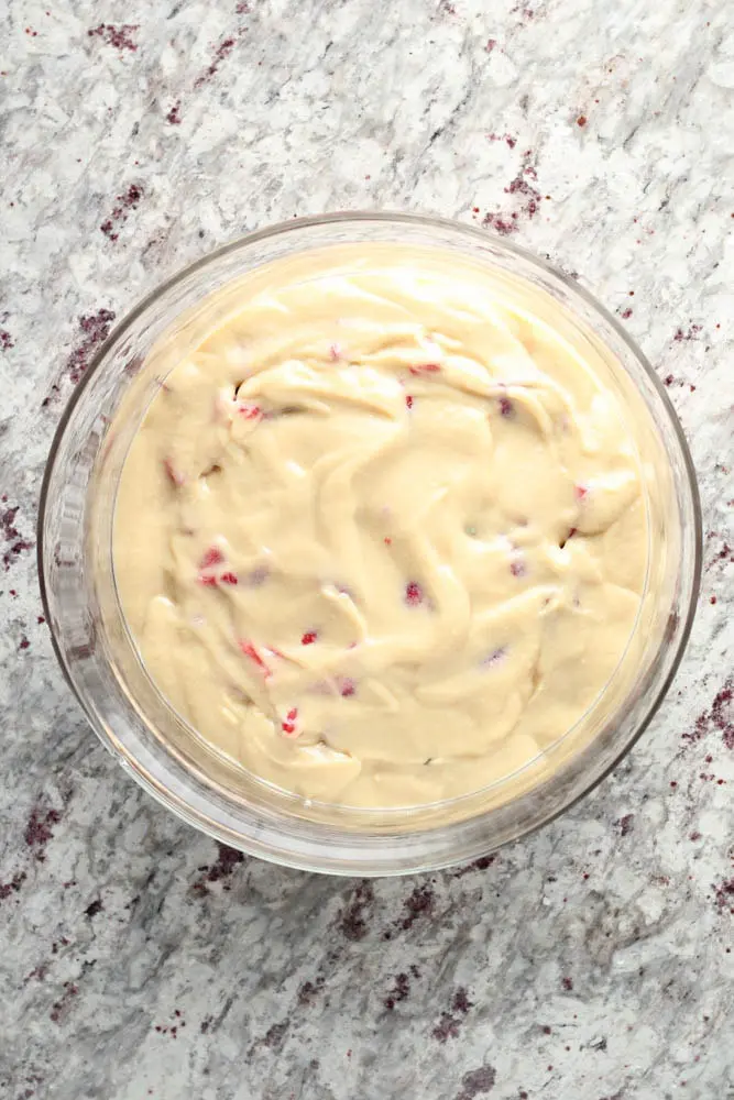 overhead view of clear round glass container filled with pale yellow vanilla pudding as the third layer in strawberry trifle