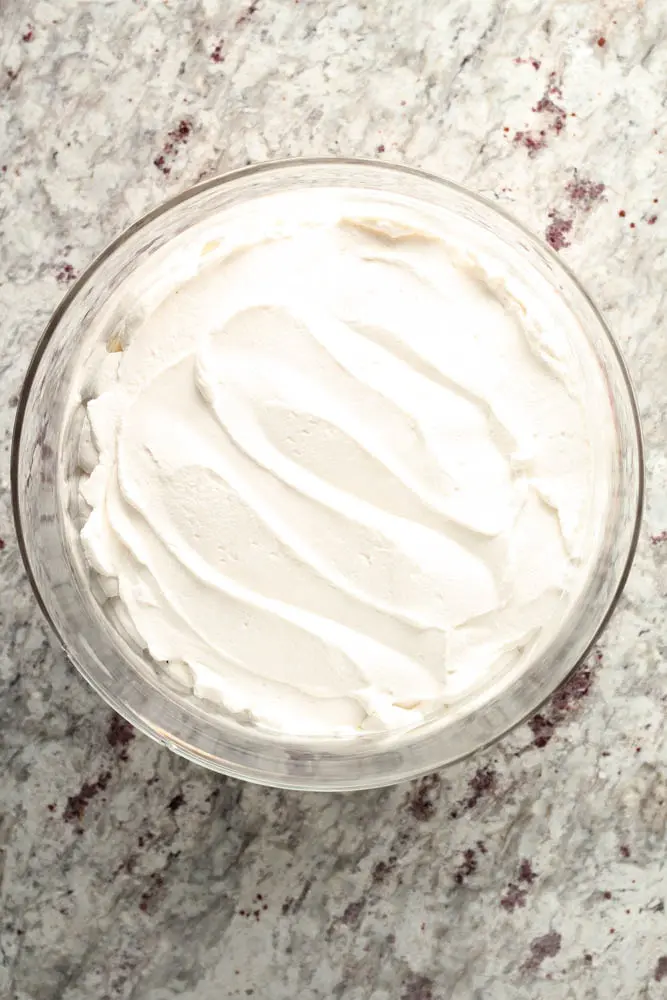 overhead look at clear round class container filled with smooth white whipped cream as the last layer of strawberry trifle