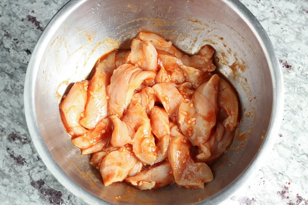 sliced raw chicken breast tossed in stainless steel bowl with chipotles in adobo, minced garlic and lime juice