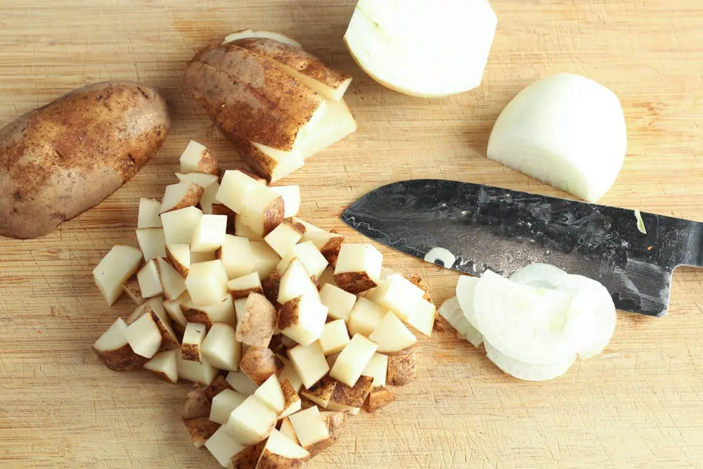 diced potato and sliced of white onion on a light wooden cutting board