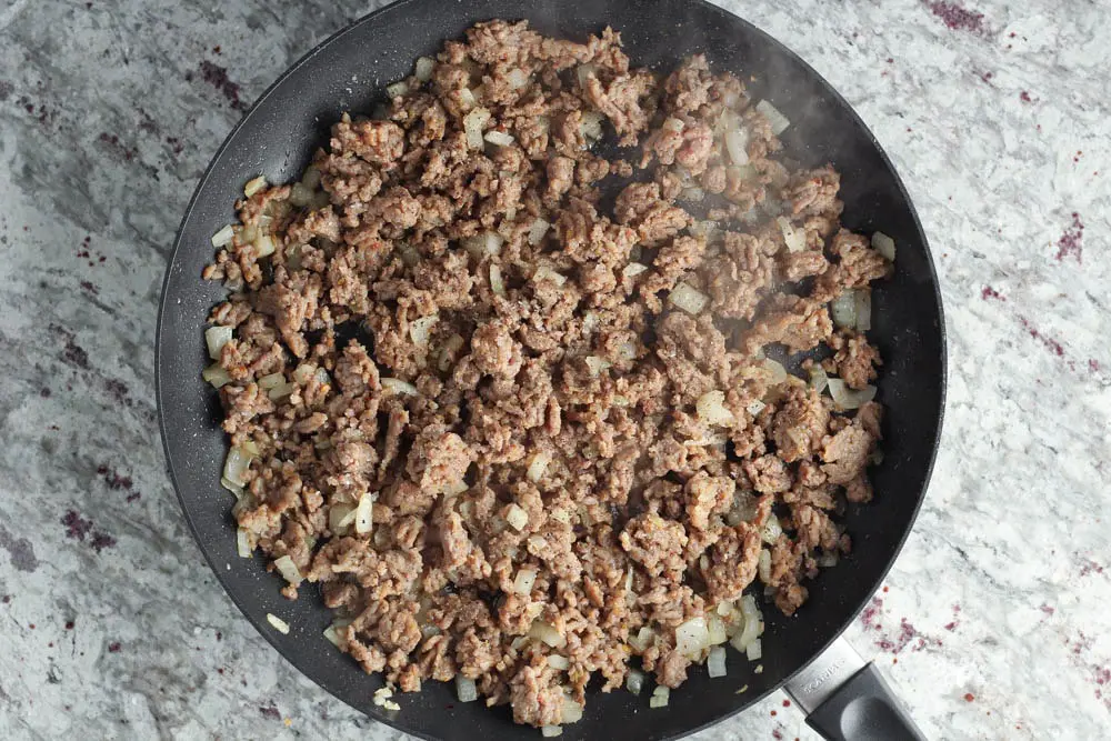 Large round black saute pan filled with cooked sausage and white onions