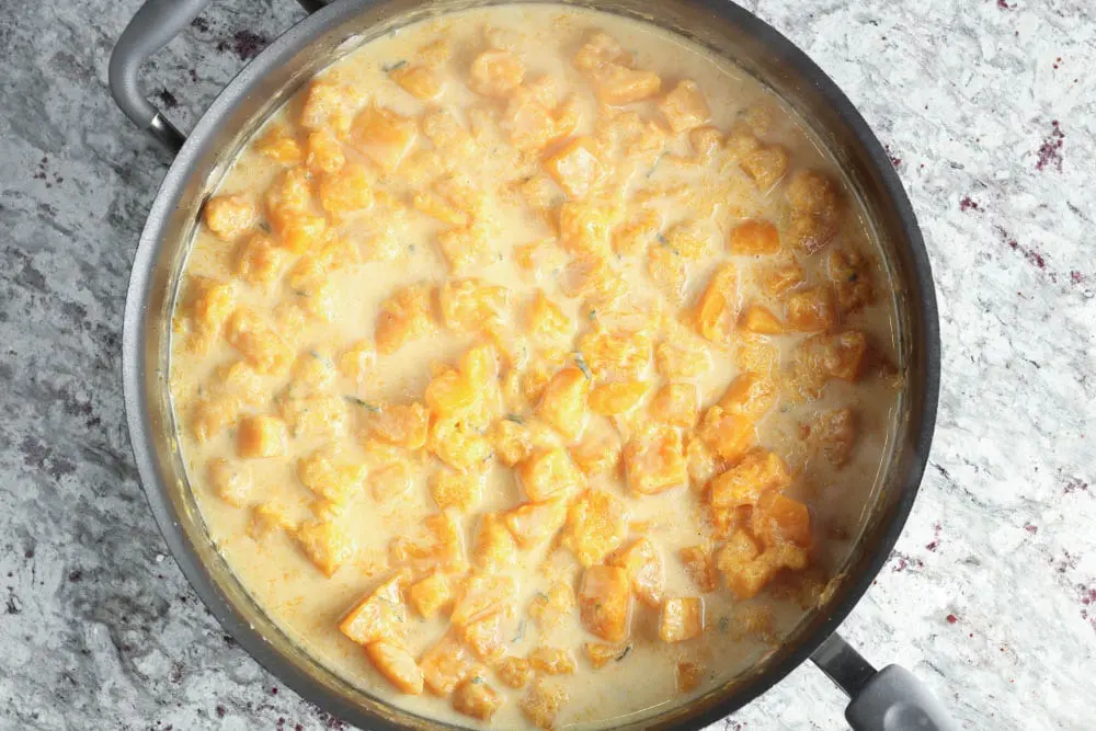 Large high rimmed saute pan filled with cooked orange butternut squash in a mixture of chicken stock and heavy cream