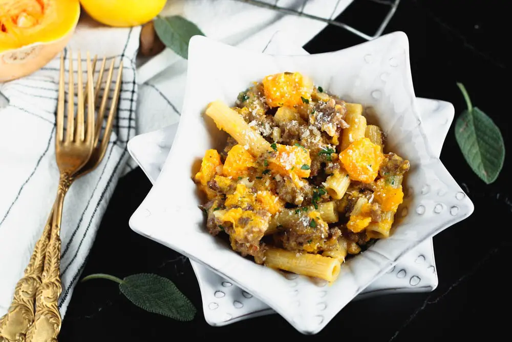 White star shaped bowl filled filled with orange butternut squash cubes, sausage pieces, rigatoni and fleck of white parmesan cheese and green chopped parsley