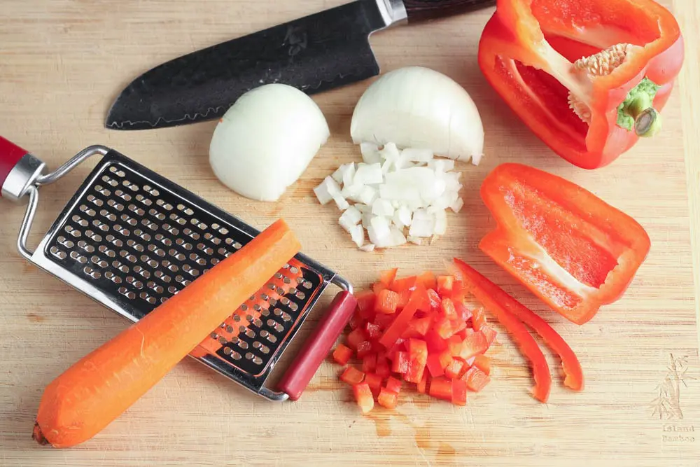 orange carrot, red bell pepper and white onion on a light wooden cutting board being prepared for recipe