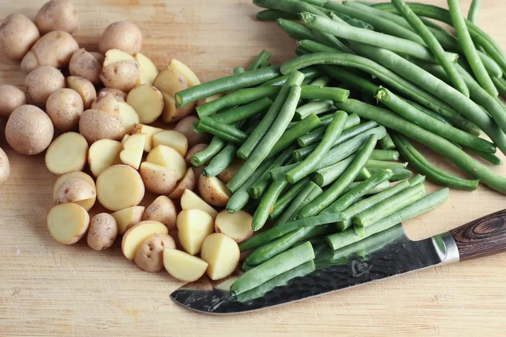 Light wooden cutting board with green beans and potatoes split in half