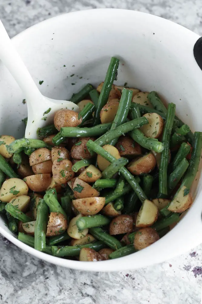 White mixing bowl filled with green beans and halved potatoes covered in a herb oil