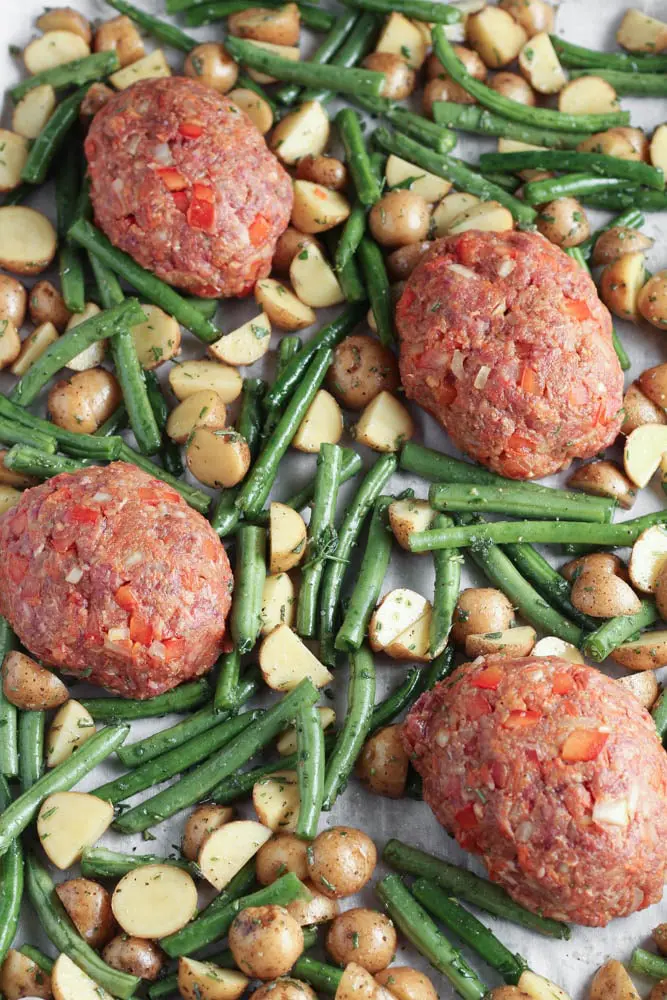 raw meatloaves on a piece of white parchment paper surrounded by green beans and potatoes