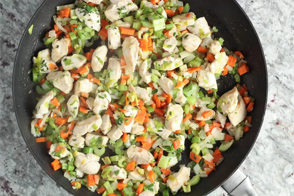 Diced chicken, carrots, celery, onions and parsley in a black saute pan