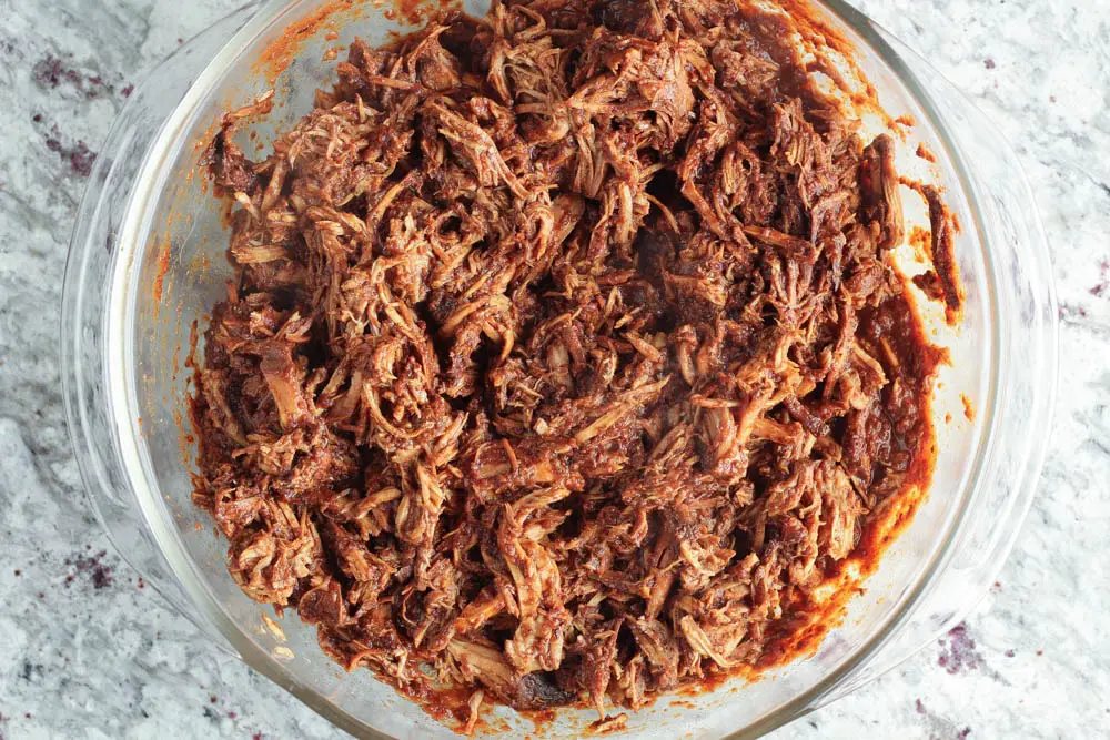 shredded pork shoulder covered in red mole sauce in a clear glass bowl